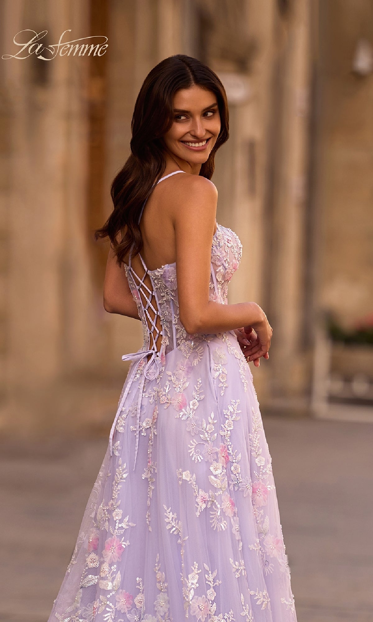 Wearing the Long Prom Dress: La Femme 32695 in light purple with floral lace embroidery, a woman stands outdoors and smiles over her shoulder.